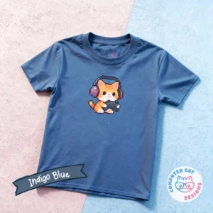An indigo blue-colored t-shirt on a pink and blue surface featuring a pixelated graphic of a cat playing videogames, with a controller in it's paws and red headphones on. The shirt has a Computer Cat Designs logo.